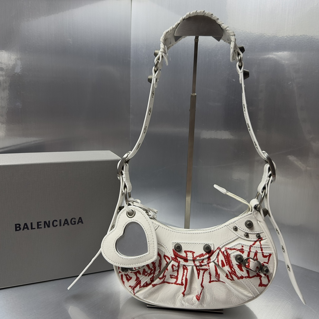 Balenciag Le Cagole半月牙腋下包涂鸦饺子包致敬经典机车包系列重磅新款王炸登场la 在传统的机车包上做了改良 可调节编织肩带附加孔眼和外挂皮革卡包 心型挂镜 沿用经典机车元素 细节非常讲究 上身简直痴迷复古率性 充满摇滚气息的大胆与前卫 辣妹本辣必须人手一个 爱了 尺寸 长26X高16X宽10CM