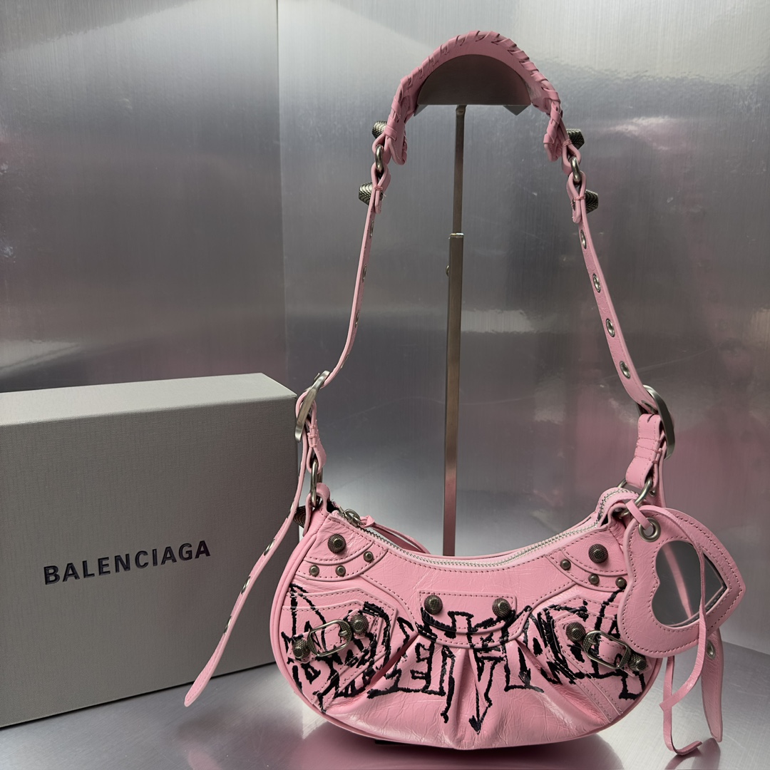 Balenciag Le Cagole半月牙腋下包涂鸦饺子包致敬经典机车包系列重磅新款王炸登场la 在传统的机车包上做了改良 可调节编织肩带附加孔眼和外挂皮革卡包 心型挂镜 沿用经典机车元素 细节非常讲究 上身简直痴迷复古率性 充满摇滚气息的大胆与前卫 辣妹本辣必须人手一个 爱了 尺寸 长26X高16X宽10CM