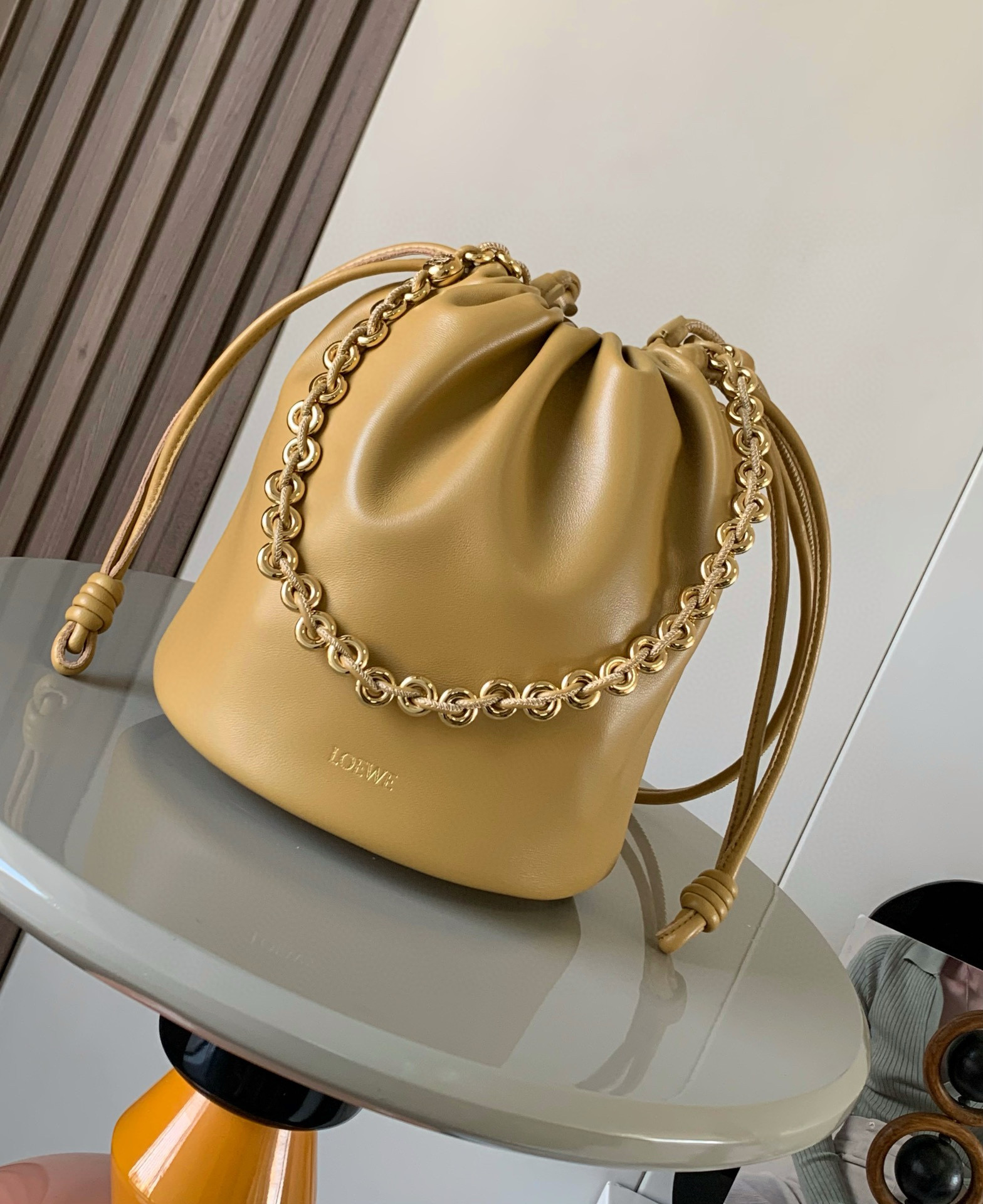 新款柔软纳帕羊皮革 Flamenco Purse Bucket 水桶手袋新品 Flamenco Purse 手袋采用褶皱设计 侧面搭配标志性绳结等关键细节Bucket 水桶手袋推出适合日常使用的全新尺寸 同时保留此系列的柔美风格 款式时尚百搭 可搭配甜甜圈链条肩背 或搭配皮革肩带斜挎 此版本采用柔软纳帕羊皮革制成  可肩背 斜挎或手提 可拆卸可调节皮革肩带  可拆卸甜甜圈链条饰有 Anagram 镌刻卵石纹 低调的磁扣开合 绒面革衬里  L O E WE 烫金或烫银 尺寸 32cm 17cm 24cm款号 9062颜色 沙漠黄