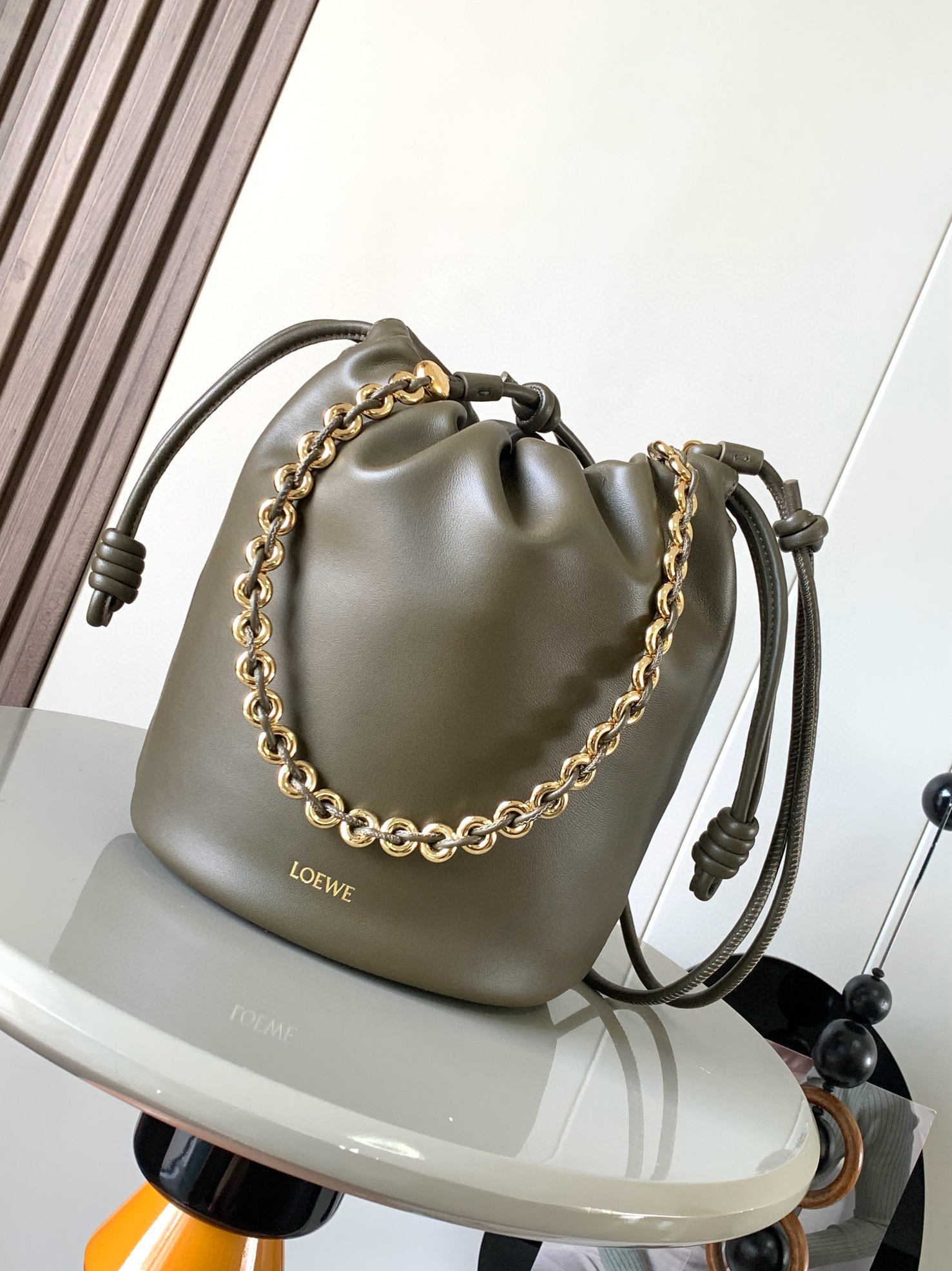 新款柔软纳帕羊皮革 Flamenco Purse Bucket 水桶手袋新品 Flamenco Purse 手袋采用褶皱设计 侧面搭配标志性绳结等关键细节Bucket 水桶手袋推出适合日常使用的全新尺寸 同时保留此系列的柔美风格 款式时尚百搭 可搭配甜甜圈链条肩背 或搭配皮革肩带斜挎 此版本采用柔软纳帕羊皮革制成  可肩背 斜挎或手提 可拆卸可调节皮革肩带  可拆卸甜甜圈链条饰有 Anagram 镌刻卵石纹 低调的磁扣开合 绒面革衬里  L O E WE 烫金或烫银 尺寸 32cm 17cm 24cm款号 9062颜色 卡其绿